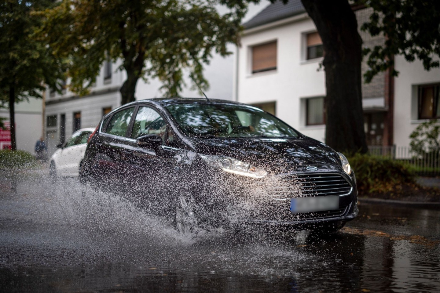 Nach starken Regenfällen am Dienstagmorgen fährt ein Auto durch eine große Pfütze in Duisburg.