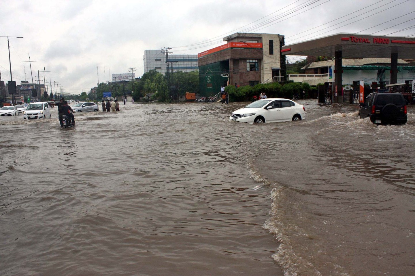 Pendler fahren in Lahore eine überschwemmte Straße entlang.